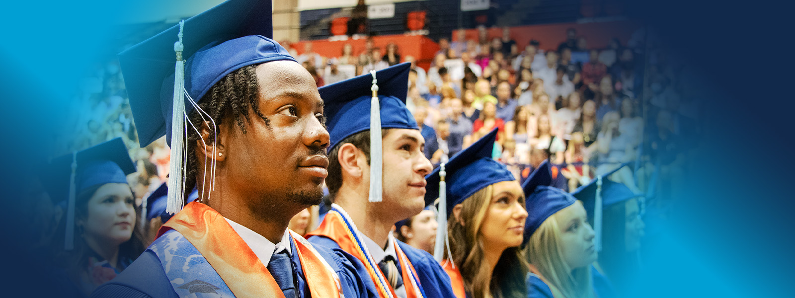College of Education graduates sitting in a row during the 2023 graduation ceremony with blue graduation caps and gowns, orange stoles, and and white tassels.