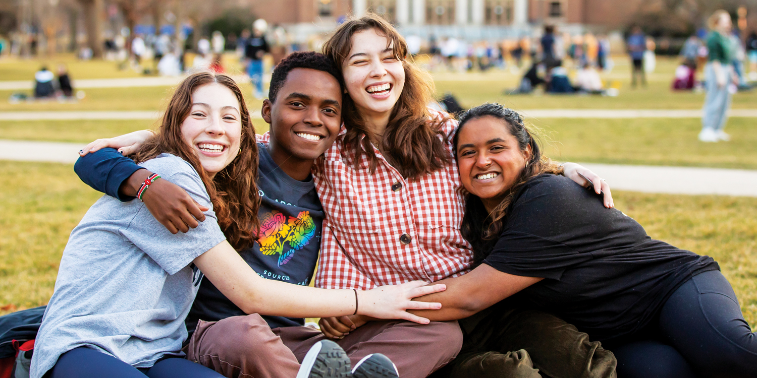 Four students hugging as they sit on the quad lawn