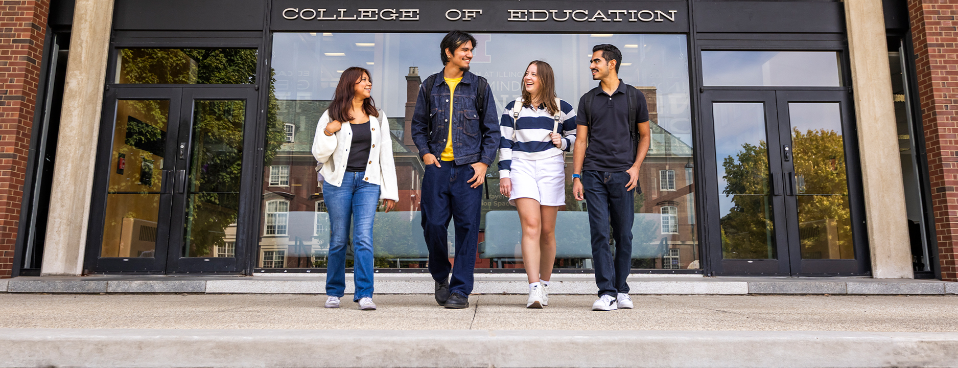 four students standing side-by-side in front of the education building
